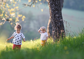 Zwei kleine Mädchen laufen über eine grüne Wiese mit Baum